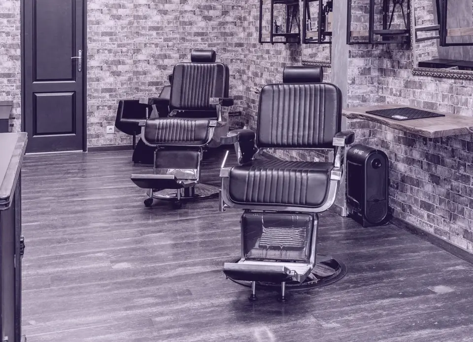 An empty barbershop with two leather chairs against a brick wall