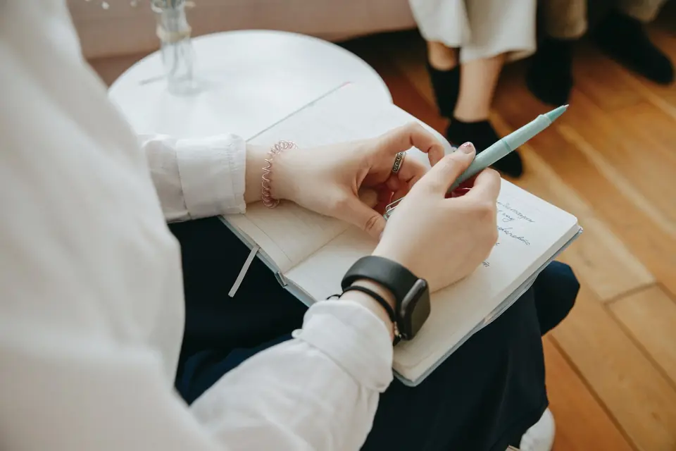 Hands writing notes in a notebook on a lap