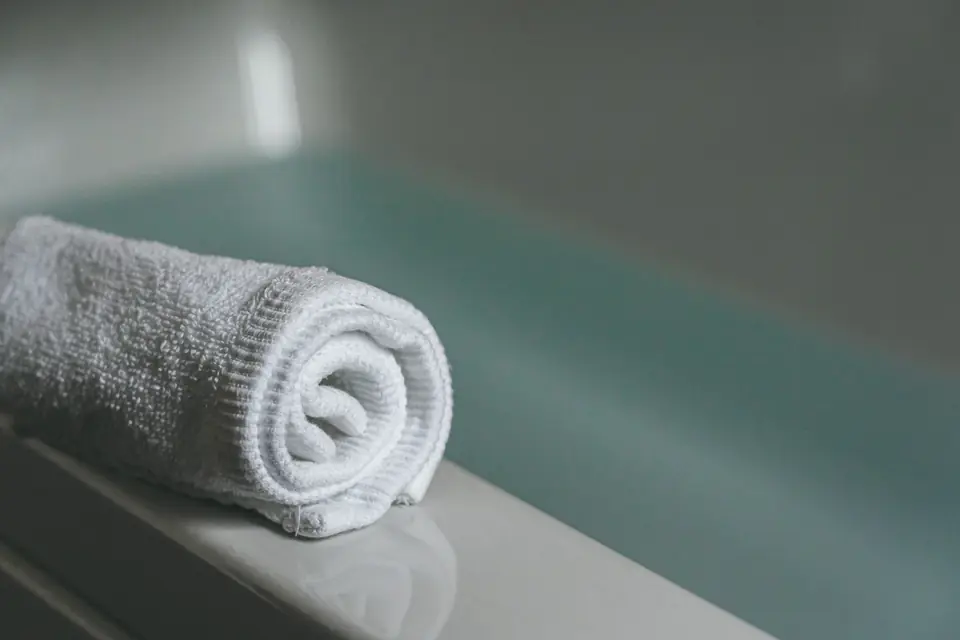 A rolled white towel on the edge of a bath of pale green water