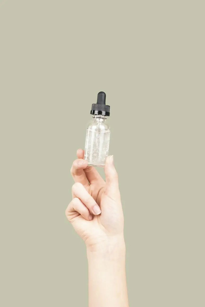 A hand holding up a small clear dropper bottle