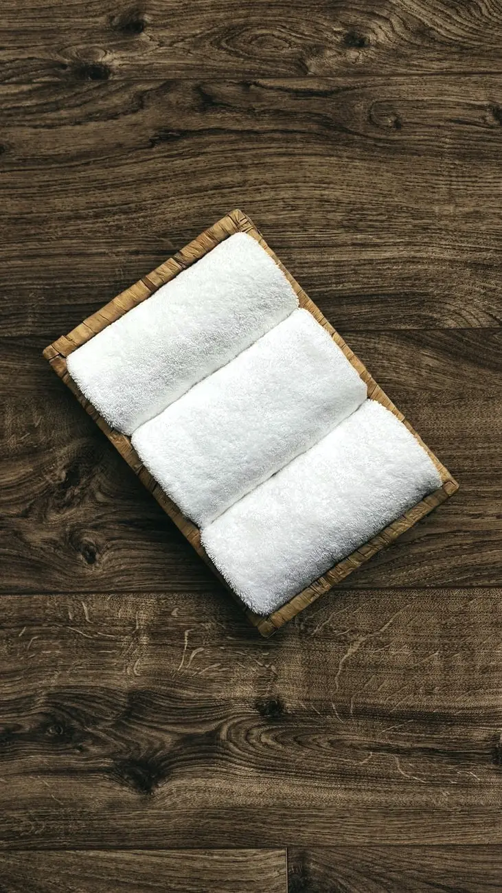 Three rolled white towels in a wooden tray on dark wood