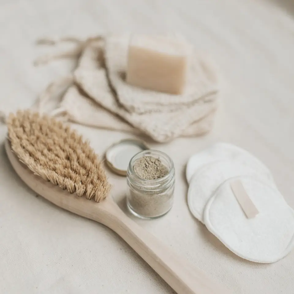 A wooden brush, cotton pads, a bar of soap and an open jar of powder on linen