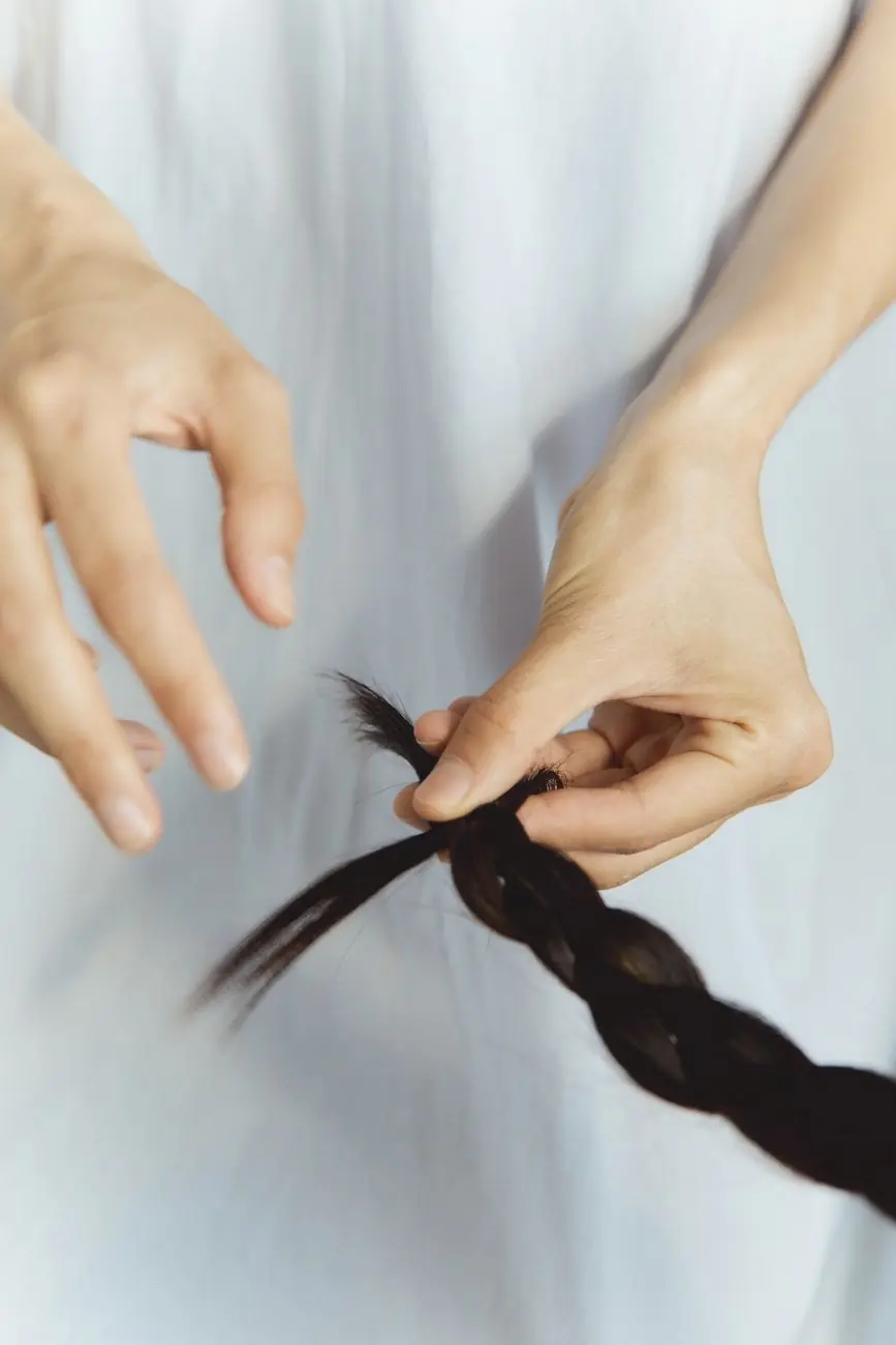 Fingers crossing strands into a braid against a pale background
