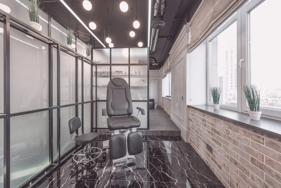 An empty salon chair in a glass room beside a row of windows