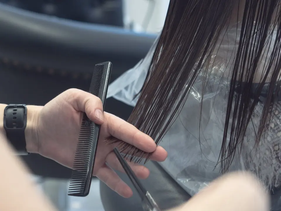 A stylist holding a comb and scissors over a wet section of dark hair