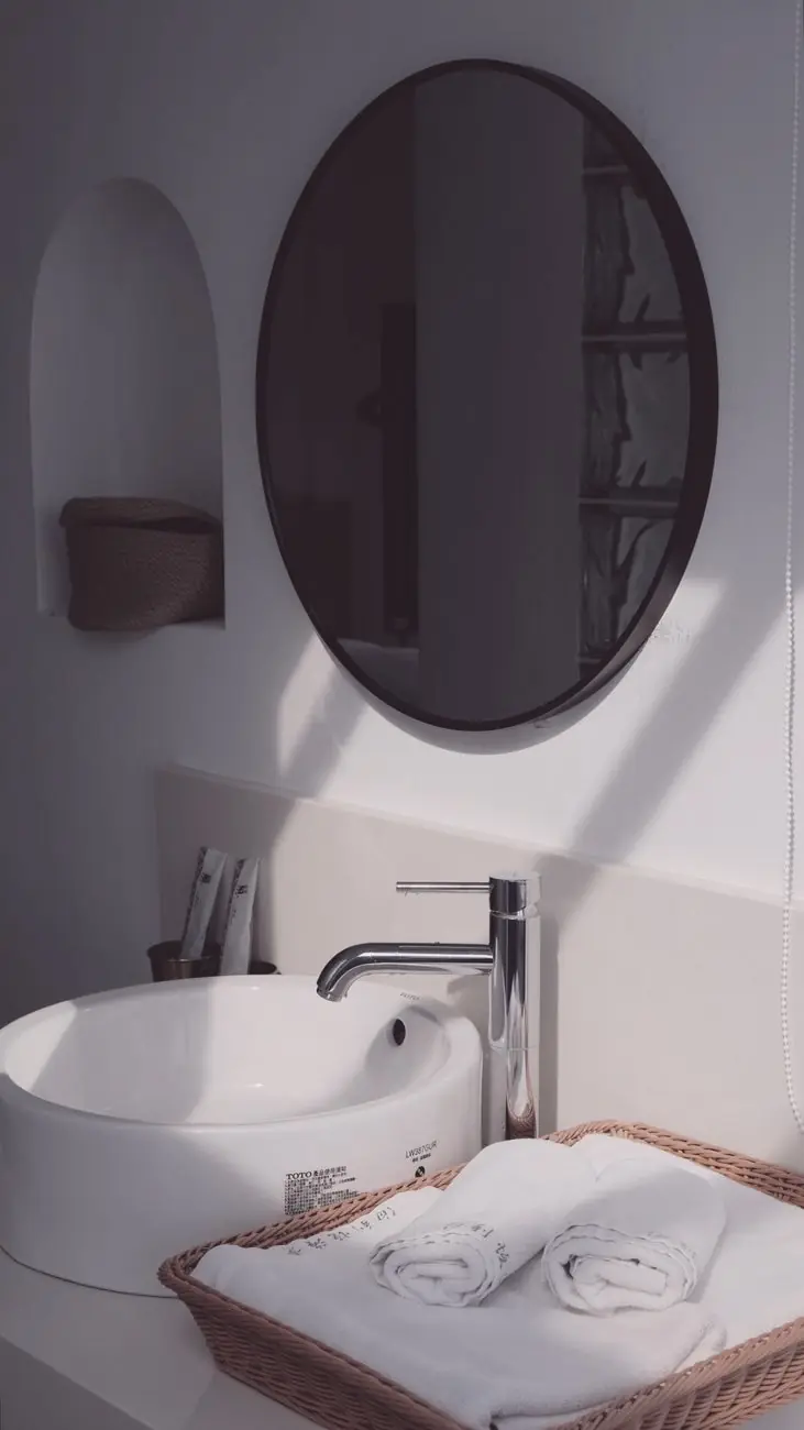 A washbasin beneath an oval mirror, with towels in a basket
