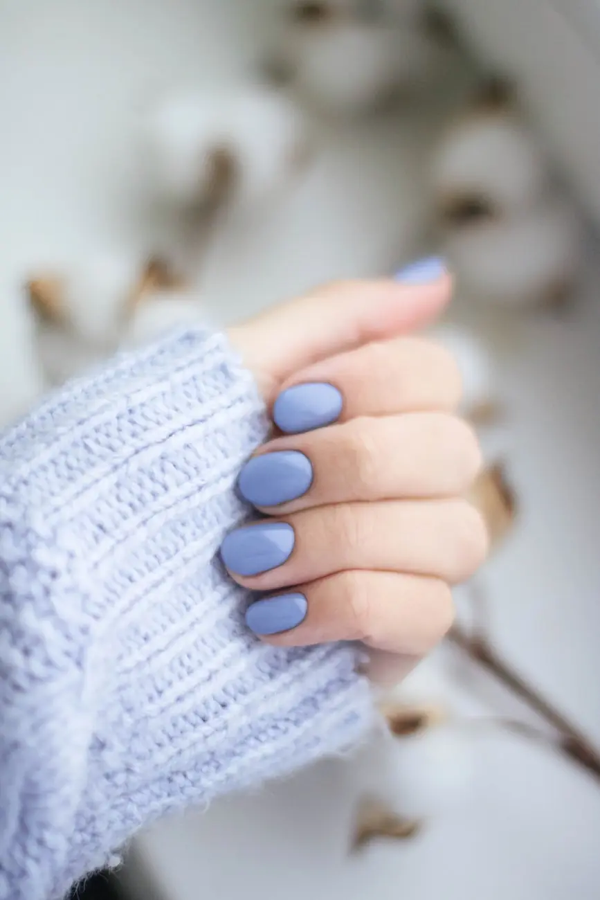 A hand with pale blue rounded nails against a knitted sleeve