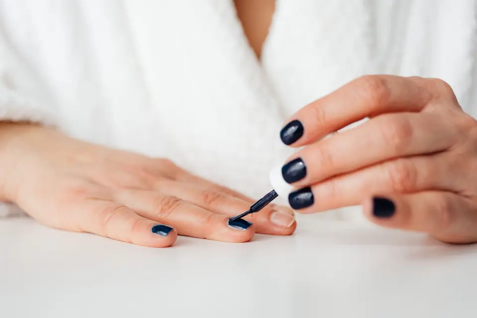 A brush painting navy polish onto short nails on a white table