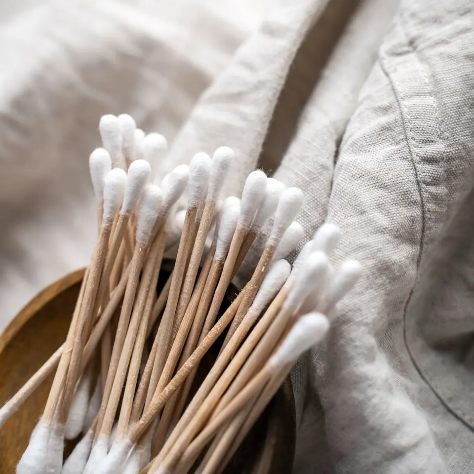 Cotton buds standing in a wooden bowl beside linen