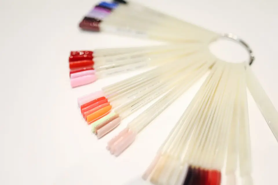 A fan of practice nail tips swatched in reds, pinks and corals